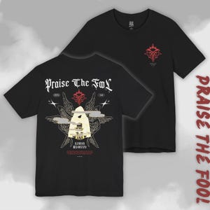 May include: Black t-shirts with the text "Praise The Fool" in a gothic font. One shirt features a red and white graphic on the front and back. The back design includes a stylized figure, wings, and additional text.