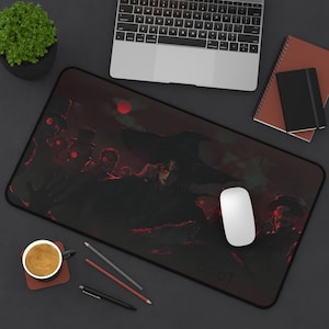 May include: A black rectangular mousepad featuring a dark, dramatic illustration with red accents and figures. A laptop, mouse, and other office supplies are arranged around the mousepad on a dark surface.