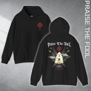 May include: Black hooded sweatshirt with a front and back graphic design. The front features a red emblem, while the back displays the text "Praise The Fool" with a detailed illustration of a figure with wings and additional text.