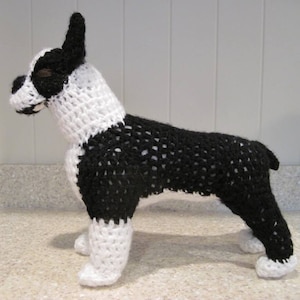 May include: A crocheted Boston Terrier dog toy, black and white with a white face and black ears, standing on a white surface.