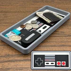 May include: A gray and black Nintendo Entertainment System (NES) themed tray with a black Jeep key fob, a pack of Listerine Cool Mint mouthwash, a few coins, and a money clip with cash inside.