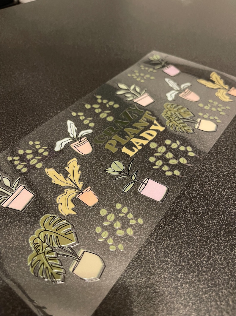 May include: A clear sticker sheet with gold foil lettering that reads "Crazy Plant Lady". The sticker sheet features various illustrations of potted plants in green, yellow, and pink.