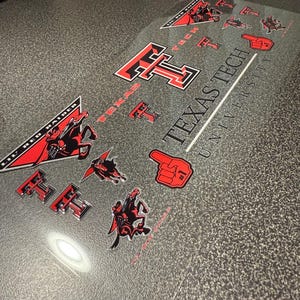 Könnte beinhalten: Eine Sammlung klarer Aufkleber mit Logos und Bildern der Texas Tech University. Die Aufkleber enthalten das Texas Tech "T"-Logo in Rot und Schwarz, das Maskottchen "Lil' Red Raider" und rote Schaumstoff-Finger-Grafiken. Die Worte "Texas Tech University" sind ebenfalls sichtbar.