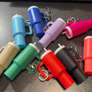 May include: A collection of ten colorful keychain bottle stoppers. The stoppers are made of a soft, flexible material and feature a variety of colors, including blue, green, red, pink, purple, and brown. Each stopper has a small loop for attaching to a keychain.