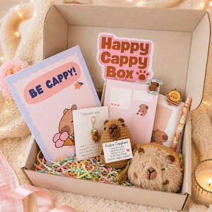 Puede incluir: Una caja de regalo "Happy Cappy Box" llena de art&iacute;culos de papeler&iacute;a, un capibara de peluche y un monedero. La caja contiene una tarjeta de felicitaci&oacute;n que dice "BE CAPPY!" y un bol&iacute;grafo con un dise&ntilde;o de capibara.