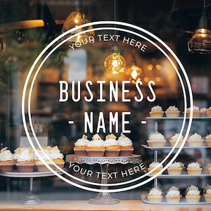 May include: A storefront window with a white circle sticker that says "YOUR TEXT HERE - BUSINESS NAME - YOUR TEXT HERE". The window is decorated with cupcakes on tiered stands.