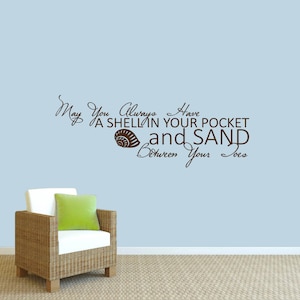 May include: A wall decal with the text "May You Always Have A Shell In Your Pocket and Sand Between Your Toes" in brown script. A seashell graphic is included. A wicker chair with a white cushion and green pillow is in the foreground.