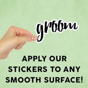 May include: A black and white sticker with the word "groom" written in a cursive font. The sticker is being held by a hand against a light green background. The text "APPLY OUR STICKERS TO ANY SMOOTH SURFACE!" is written below the sticker.