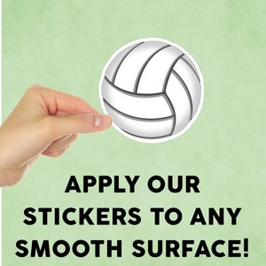 May include: A white volleyball sticker with black lines. The sticker is being held by a hand. The text "APPLY OUR STICKERS TO ANY SMOOTH SURFACE!" is below the sticker.