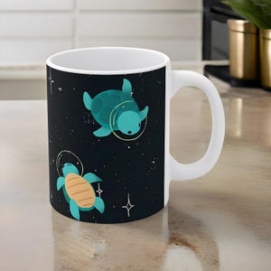 May include: White ceramic mug with a black background and a design of two green sea turtles wearing astronaut helmets floating in space. The turtles are surrounded by white stars.
