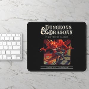 May include: A rectangular black mousepad featuring the Dungeons & Dragons logo, the text "DUGEON MASTERS RULEBOOK" and "FANTASY ROLE-PLAYING GAME," and a central illustration of a red dragon battling a warrior with a sword and shield.