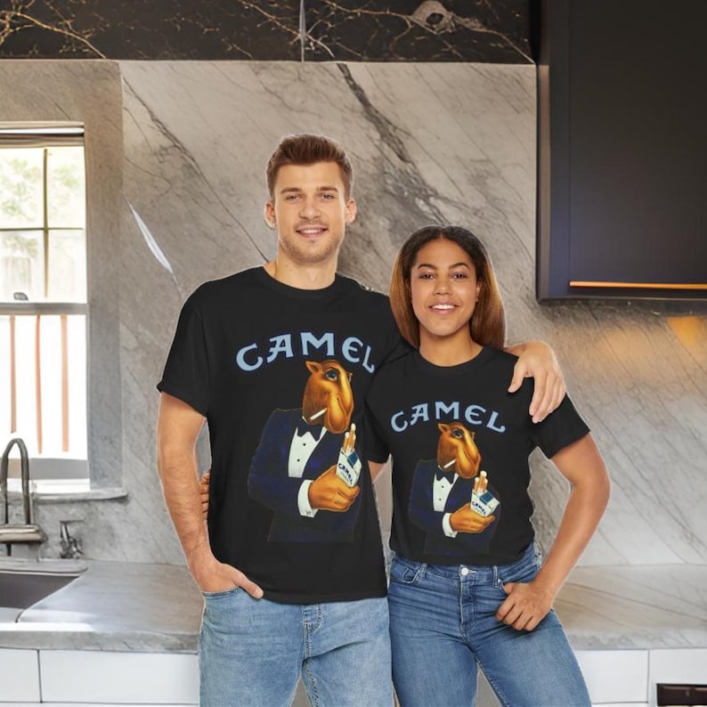 May include: Two people wearing black t-shirts with a vintage Camel cigarette ad featuring a cartoon camel in a tuxedo. The ad text reads "Camel".