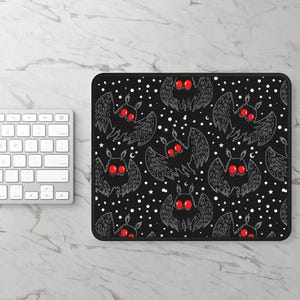 May include: Black mouse pad with a repeating pattern of white moths with red eyes on a black background. The moths are flying against a background of white stars and crescent moons.