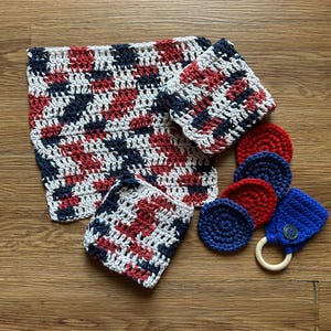 Könnte beinhalten: Ein Set aus gehäkelten Artikeln, bestehend aus einem großen quadratischen Tuch, zwei kleineren quadratischen Tüchern, vier runden Pads in Rot und Blau sowie einem blauen Häkelteil an einem Holzring mit grünem Knopf.