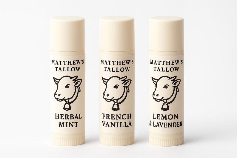 K&ouml;nnte beinhalten: Drei beigefarbene Lippenbalsam-Tuben mit wei&szlig;en Kappen. Jede Tube hat eine schwarz-wei&szlig;e Kuh-Illustration und den Text "MATTHEW'S TALLOW". Die Geschmacksrichtungen sind "HERBAL MINT", "FRENCH VANILLA" und "LEMON & LAVENDER".