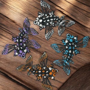 May include: Four decorative butterflies made of black, white, purple, blue, and orange beads. The butterflies are arranged on a wooden surface.