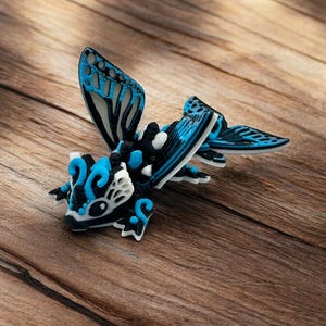 May include: A blue, black, and white 3D puzzle of a dragon with wings. The dragon is posed with its wings spread and its head tilted down.