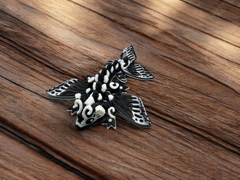 May include: A black and white 3D printed figurine of a fish with intricate details. The fish has large wings and a detailed face.
