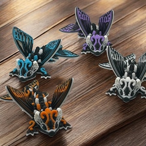 May include: Four small, intricately detailed, hand-painted figurines of winged creatures with black, white, orange, blue, and purple accents. The figurines are arranged on a wooden surface.