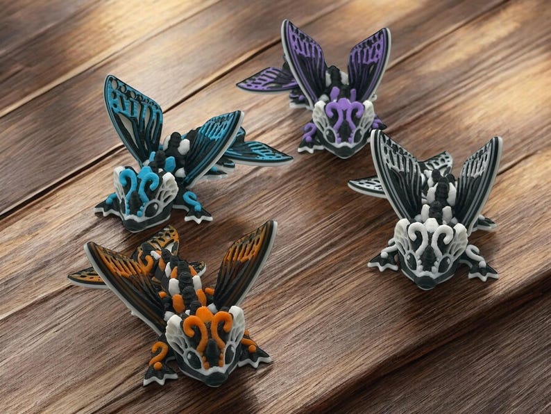 May include: Four small, intricately detailed, hand-painted figurines of winged creatures with black, white, orange, blue, and purple accents. The figurines are arranged on a wooden surface.