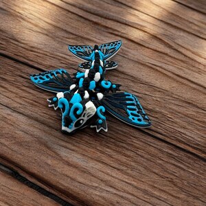 May include: A blue, black, and white 3D printed dragon figurine with intricate wings. The dragon is posed with its wings spread out and its head tilted down.