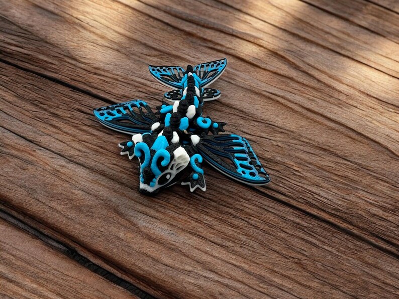 May include: A blue, black, and white 3D printed dragon figurine with intricate wings. The dragon is posed with its wings spread out and its head tilted down.