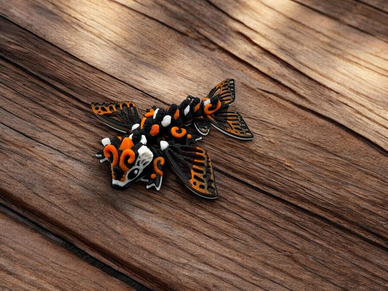 May include: A black, orange, and white decorative figurine of a stylized fish with wings. The figurine is made of a textured material and has intricate details.