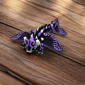 May include: A purple and black dragon figurine with intricate details and white accents. The dragon has wings and a long tail.