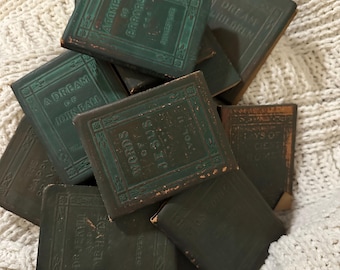 Pode incluir: Uma coleção de livros antigos com capas verde-escuras. Os títulos incluem "A Dream of John Ball", "Words of Jesus, Vol. 11" e "A Compdy of Errors". Os livros estão empilhados sobre uma superfície branca texturizada.