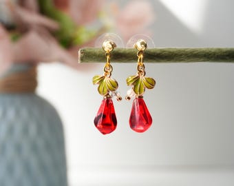 May include: A pair of gold earrings with red teardrop-shaped glass beads and green enamel leaves.