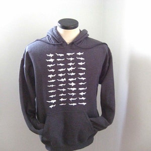 Op de afbeelding: Een donkergrijze hoodie met een witte grafische print van een herhalend patroon van haaien.
