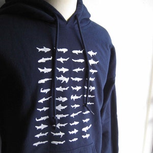 May include: A navy blue hooded sweatshirt with a white graphic print of a school of fish. The sweatshirt has a drawstring hood and a kangaroo pocket.