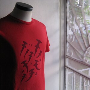 May include: Red t-shirt with a graphic print of multiple hammerhead sharks in black.