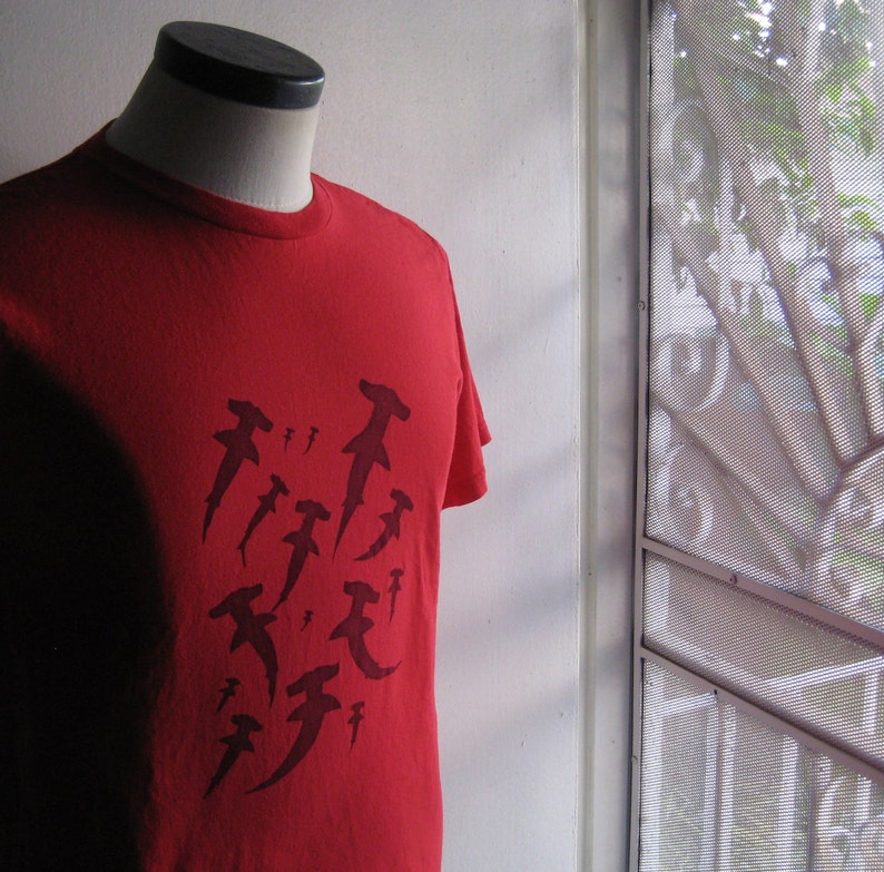 May include: Red t-shirt with a graphic print of multiple hammerhead sharks in black.