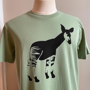 May include: A green t-shirt with a black silhouette of an okapi, a type of African mammal.