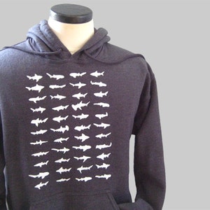 Op de afbeelding: Een donkergrijs hoodie met een witte grafische print van een school haaien.
