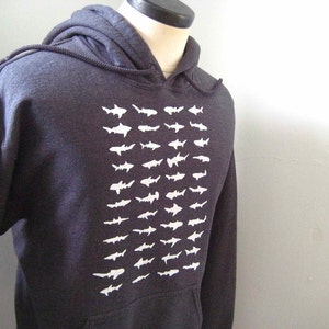 Op de afbeelding: Een donkergrijs hoodie met een witte grafische print van een herhalend patroon van haaien.