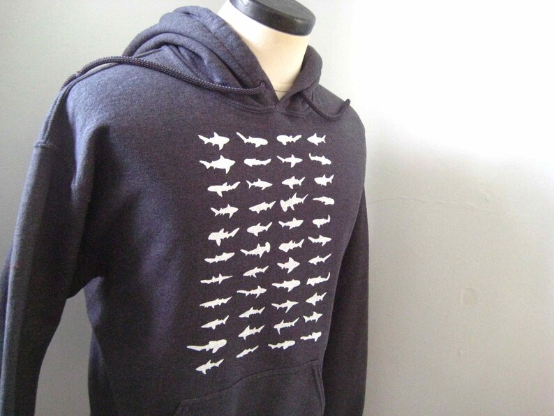 Op de afbeelding: Een donkergrijs hoodie met een witte grafische print van een herhalend patroon van haaien.