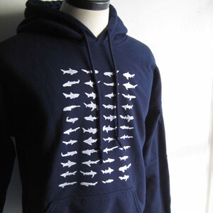 May include: A navy blue hoodie with a white graphic of a school of fish. The hoodie has a drawstring hood and a kangaroo pocket.