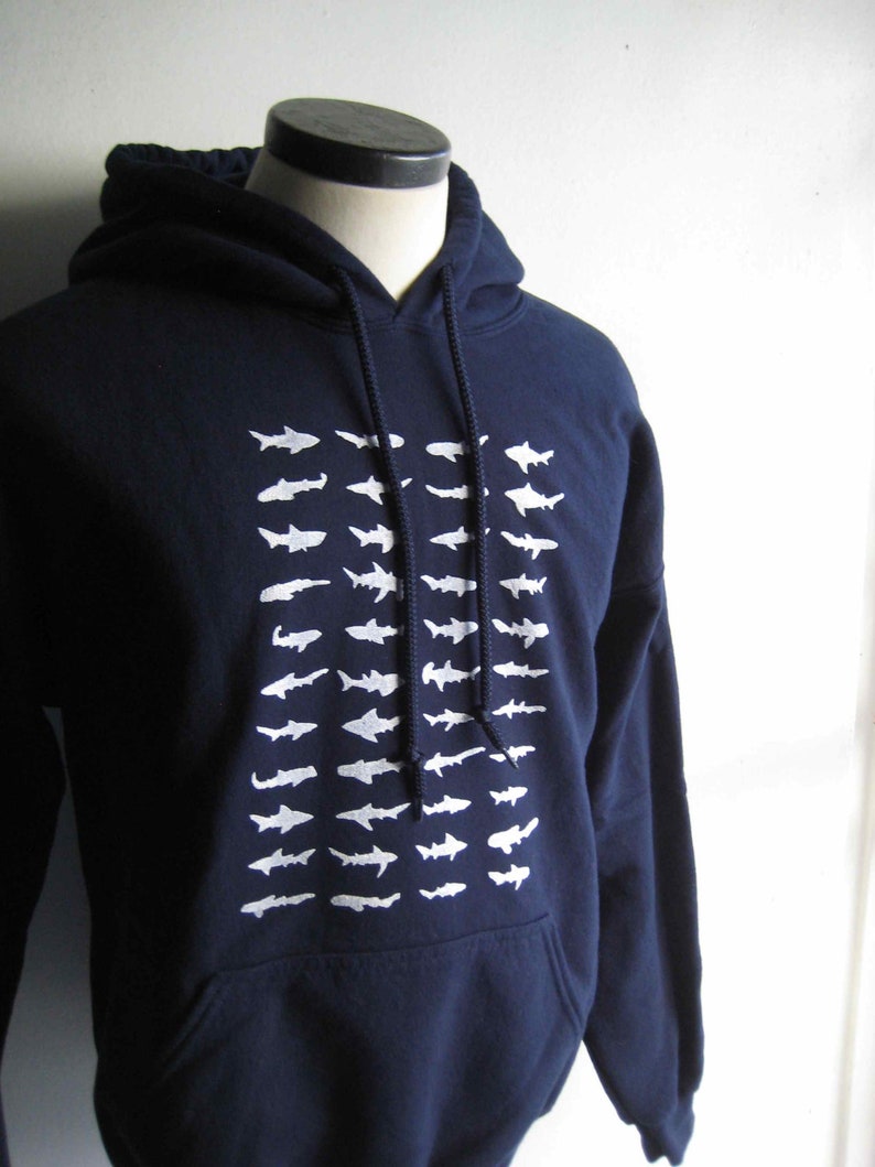 May include: A navy blue hoodie with a white graphic of a school of fish. The hoodie has a drawstring hood and a kangaroo pocket.