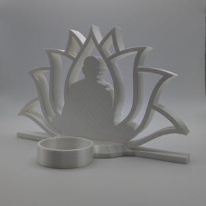 May include: White 3D printed candle holder shaped like a lotus flower with a Buddha silhouette in the center. The holder has a small round space for a tea light candle.