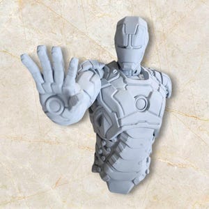 May include: A grey, 3D-printed bust of Iron Man in a stopping pose. The sculpture features detailed armour plating and a helmet with a distinct design. The hand is extended, with the palm facing forward. The bust is a collectible item.