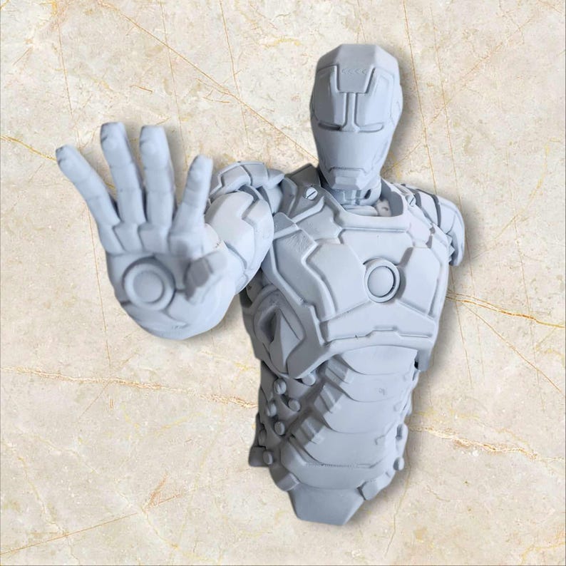 May include: A grey, 3D-printed bust of Iron Man in a stopping pose. The sculpture features detailed armour plating and a helmet with a distinct design. The hand is extended, with the palm facing forward. The bust is a collectible item.