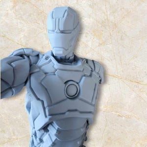 May include: A light grey Iron Man bust, showcasing the character's helmet and armour design. The bust has a detailed, textured surface and a circular chest emblem. The figure is set against a neutral background.
