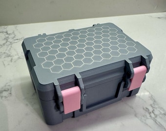 May include: A small grey storage box with a honeycomb pattern on the lid and pink latches.