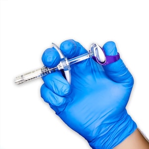 May include: A clear plastic syringe with a graduated barrel and a white plunger, featuring a purple ergonomic finger grip attachment secured to the plunger end, designed to assist with the manual operation of the syringe mechanism.