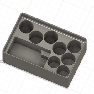 Pode incluir: Uma caixa de armazenamento de plástico cinza com sete compartimentos redondos e um compartimento retangular. A caixa é projetada para guardar objetos pequenos.