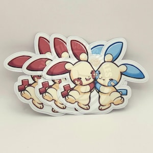 May include: Four white stickers with a red and blue cartoon character hugging. The characters are both wearing a red cross on their cheeks. The stickers are stacked on top of each other.