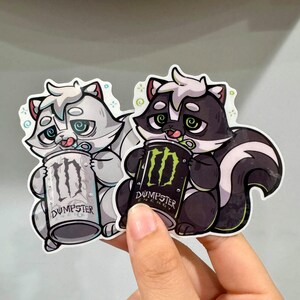May include: Two stickers featuring cartoon skunks holding energy drink cans. One skunk is gray and white, the other is black and white. The cans read "Dumpster" and have a green logo.