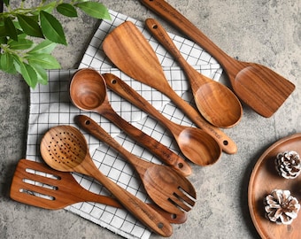 Puede incluir: Una colección de utensilios de cocina de madera, que incluye cucharas, espátulas y un tenedor, dispuestos sobre un paño a cuadros. Los utensilios son de color marrón cálido y parecen estar hechos de madera dura. Algunos utensilios tienen el texto "Parker Family" grabado en los mangos.